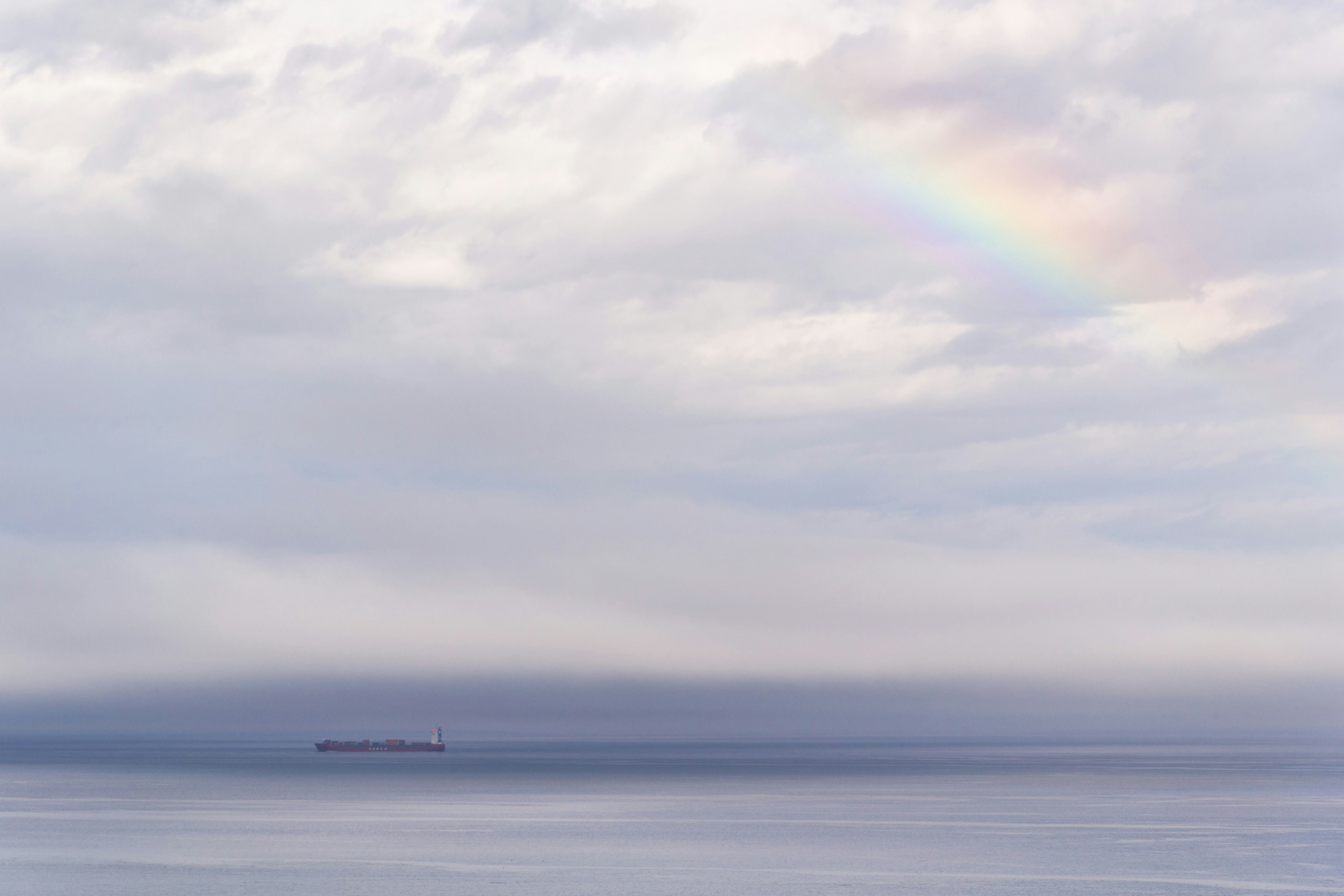 vessel on ocean under cloudy sky with rainbow